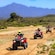 A group of riders on single seat all terrain vehicles driving single file in a desert setting